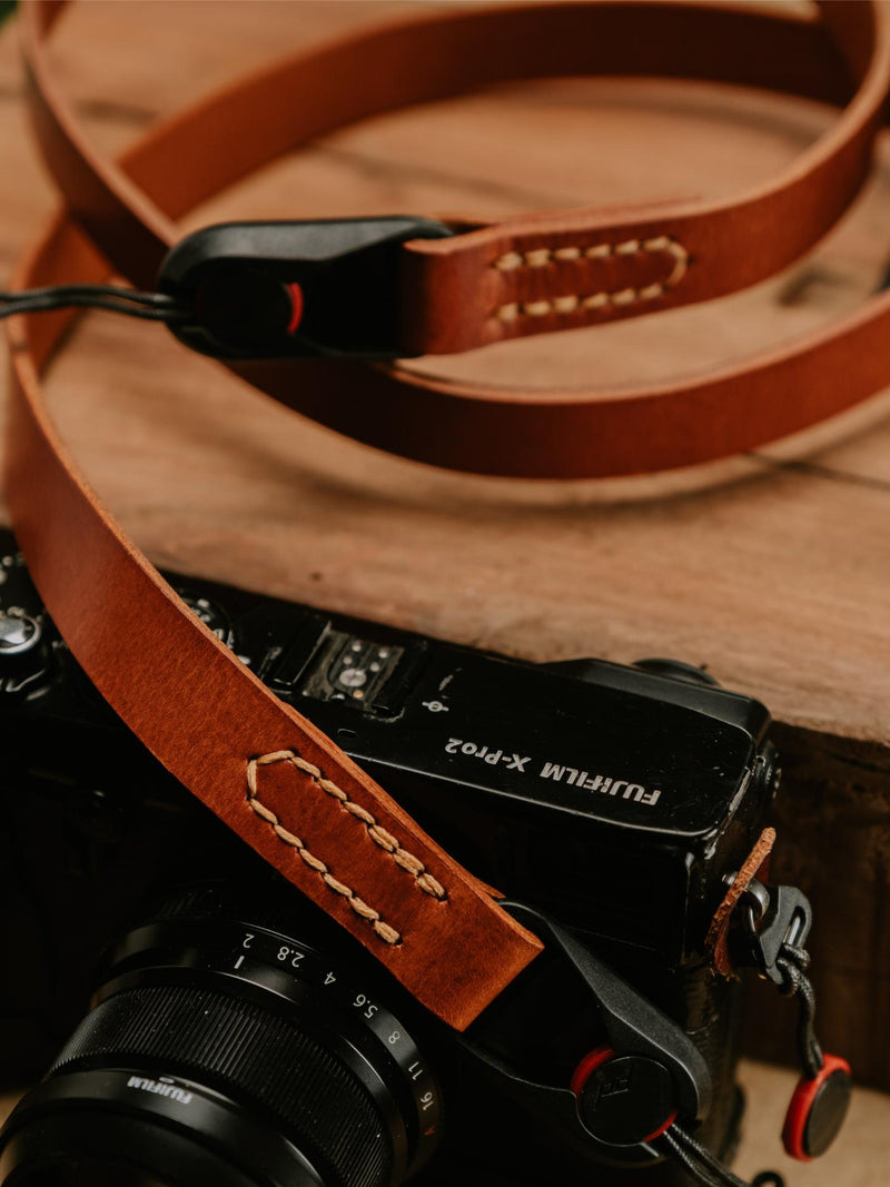 Lavietnamita hand stitch leather camera strap laying on black camera with peak design anchor link in beautul whiskey colour